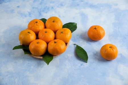 Close up photo of clementine mandarins on wooden plate over blue backgroundの写真素材