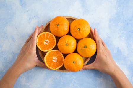 Female hands taking wooden board full with clementine mandarinsの写真素材