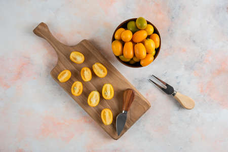 Whole kumquats in bowl and half cut kumquats on wooden cutting boardの写真素材
