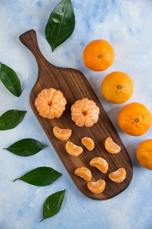 Peeled fresh mandarin slices on wooden board with whole mandarinsの写真素材