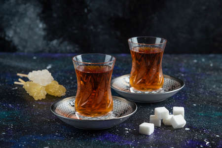 Glass of tea with sugar and candy on blue backgroundの写真素材