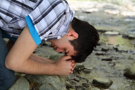 Close-up of man kneeling and praying by a creekの写真素材