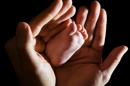 Loving hands gently embracing infant foot, black backgroundの写真素材