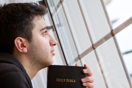 Young man looking outside with Bible in hand