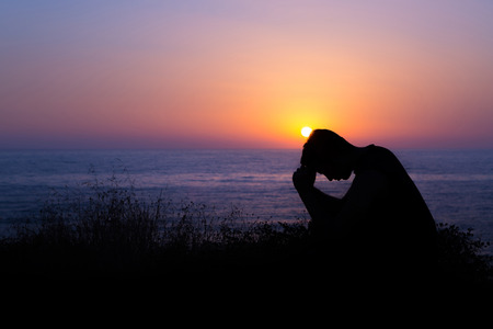 Young man praying to God during sunset by the seaの写真素材