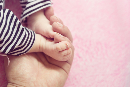 Adorable Little Baby Girl Feet Held by Daddy on Pink Backgroundの写真素材