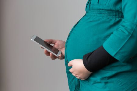 Pregnant serious woman sitting on bed using her smartphone