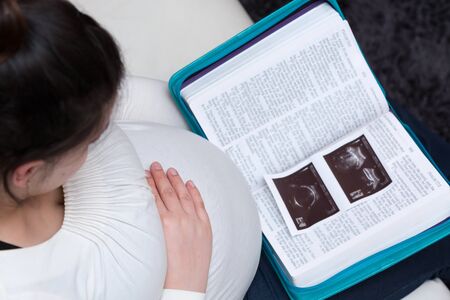 Young expectant mom reading her Bible and looking at baby ultrasound