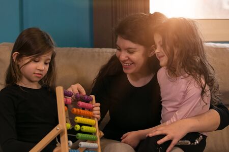 Young mother teaching her little daughters mathematics from their living room