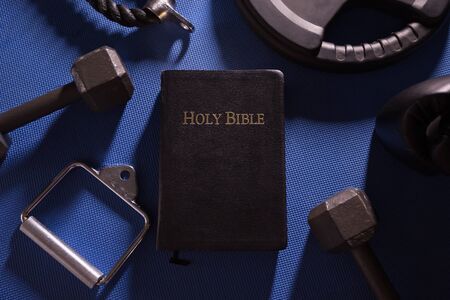 Holy Bible surrounded by dumbbells weights and other exercise equipmentの写真素材
