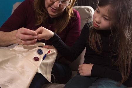 Loving Grandmother teaches her little granddaughter how to sew buttonsの写真素材