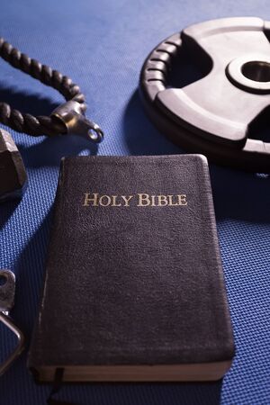 Holy Bible surrounded by dumbbells weights and other exercise equipmentの写真素材