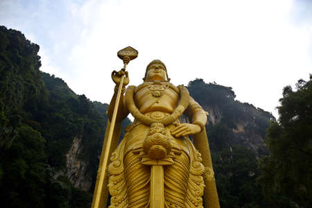 Gombak, Selangor, Malaysia 08.14.2019: Upper body part of the giant and amazingly detailed golden Murugan statue with the famous limestone hill of Batu Caves and bright sky in the backgroundのeditorial素材
