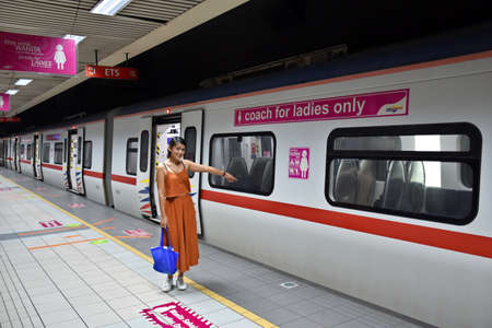 Kuala Lumpur, Malaysia, 08.14.2019: A beautiful Thai girl smiling, standing at the pink strictly for ladies zone and pointing to an empty coach for ladies at KS Sentral stationのeditorial素材