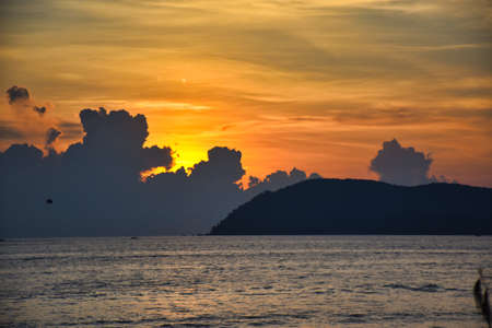 Amazing, wonderful and dramatic golden colored sky behind the clouds during a stunning sunset on a magical beach of the Island of Langkawi in Malaysiaの写真素材