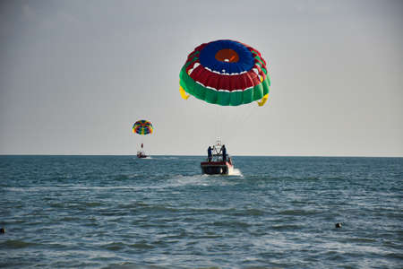 Parasailing on the waves of the azure Andaman sea under the blue sky near the shores of the sandy beautiful exotic and stunning Cenang beach in Langkawi island, in Malaysia.のeditorial素材