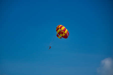 Parasailing on the waves of the azure Andaman sea under the blue sky near the shores of the sandy beautiful exotic and stunning Cenang beach in Langkawi island, in Malaysia.のeditorial素材