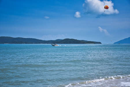Parasailing on the waves of the azure Andaman sea under the blue sky near the shores of the sandy beautiful exotic and stunning Cenang beach in Langkawi island, in Malaysia.のeditorial素材