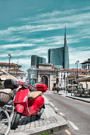 Milan, Italy 06.29.2020: An ordinary Milanese street view with a red Piaggio Vespa scooter Porta Garibaldi, Garibaldi Gate and the UniCredit Tower in the backgroundのeditorial素材