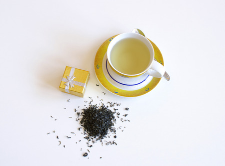 Yellow porcelain cup of tea with blue flowers, teaspoon, spill tea leaves on a white backgroundの写真素材