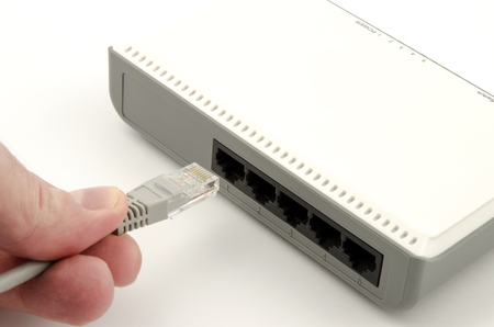 A close-up view of a finger's hand connecting a gray lan cable into the router on a white backgroundの写真素材
