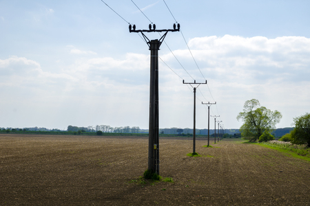 A view of a row of columns of a power line column in a landscape with trees with a field under a blue skyの写真素材
