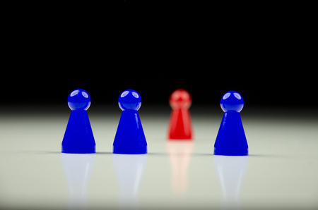 A close-up view of a row of blue figures and one red figurine unfocused in background with reflectionの写真素材
