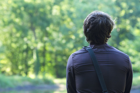 A rear view of a lonely young man sitting and looking at nature with a blurred backgroundの写真素材