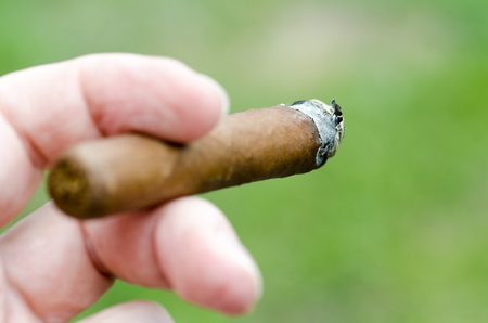 Close-up photo of a hand with fingers holding a burning cigar with blurred foregroundの写真素材