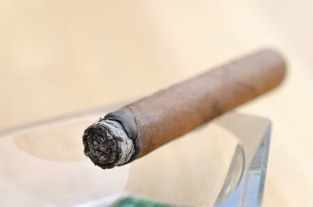 Close-up photo of a burning cigar in a glass ashtray with a blurred backgroundの写真素材