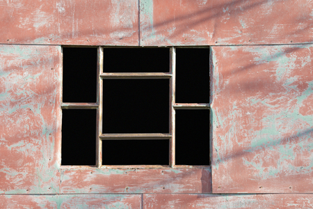 Empty window with grids on a metal structure painted red on a sunny day