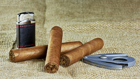 Three Cuban cigars with a lighter and a cutter on a jute backgroundの写真素材