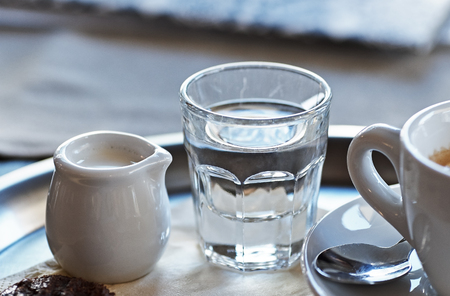 A cup of coffee with a sprig of water and milk on a tray with a biscuitの写真素材