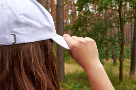 Young woman on a walk in a forest among the trees holding her hand a white baseball capの写真素材