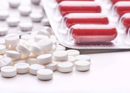 Still life with pile of round pills or tablets, antidepressants or painkillers with space for text. Red capsules in blister pack on white table top.の写真素材