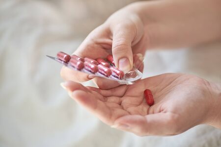 Close-up view of the hands of a sick young woman. Girl in bed holding blister and tablets or pills....