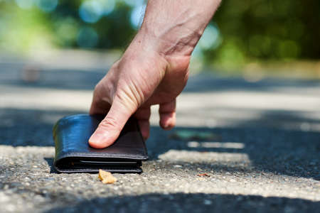 Photo of a sidewalk and the hand of a man who found a black leather wallet while walkingの写真素材
