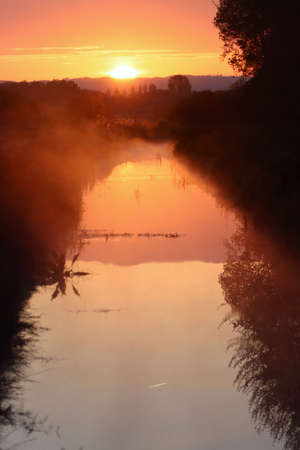 Sunrise over river with morning mist and orange skyの写真素材