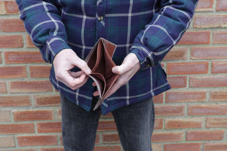 Man with no money showing empty wallet with brick wall behind