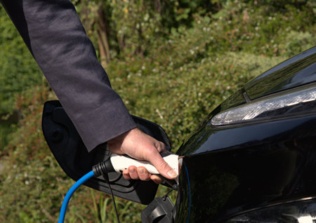 Person charging a black electric car with blue cableの写真素材