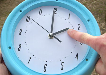 Hand adjusting the time on a clock for daylight savings