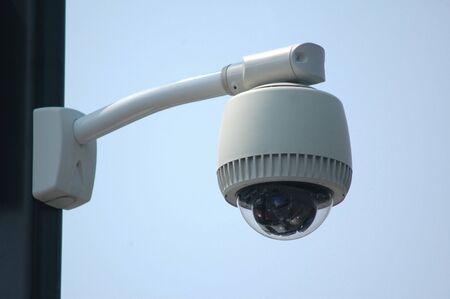 Overhead video security camera mounted on a pole, against a blue skyの写真素材