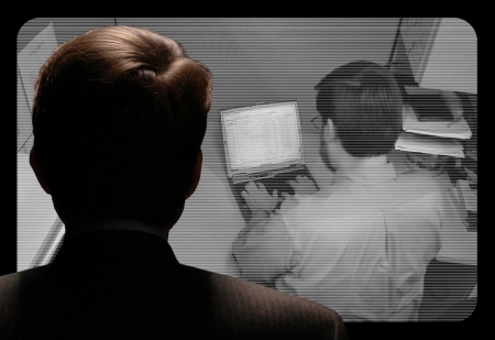 Man observing an employee work via a closed-circuit video monitorの写真素材