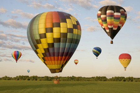 Various hot-air balloons landing in a field. One is on the ground. Others are floating.の写真素材