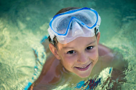 Portrait of a happy, smiling boy in the crystal, clear blue sea with a mask on his foreheadの写真素材