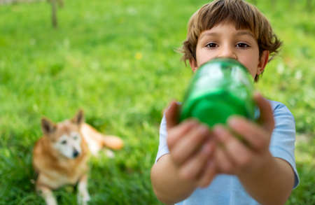 Portrait of a cute 5 year old boy drinking water from a green bottle with a big dog watching him in the backgroundの写真素材
