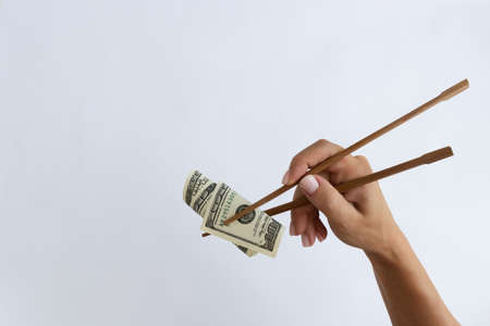 Female hand holding 100 dollars with chopsticks. On a white background with a copy space.の写真素材