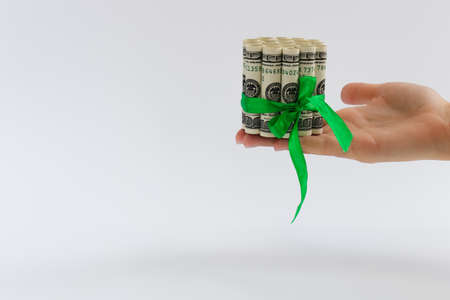 Female hand holding rolled 100 dollars banknotes tied with green gift ribbon.の写真素材