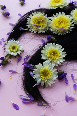 Dark hair with yellow flowers and petals on it. Hair care concept.の写真素材