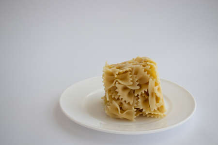 Cooked farfallini pasta in a shape of cube on a white plate. Copy space.の写真素材